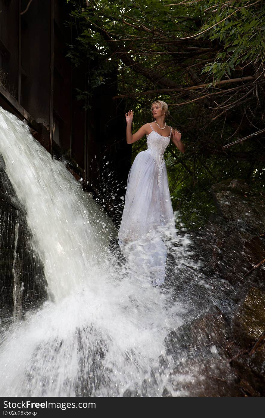 Young blonde woman in a white wedding dress near the waterfall. Young blonde woman in a white wedding dress near the waterfall