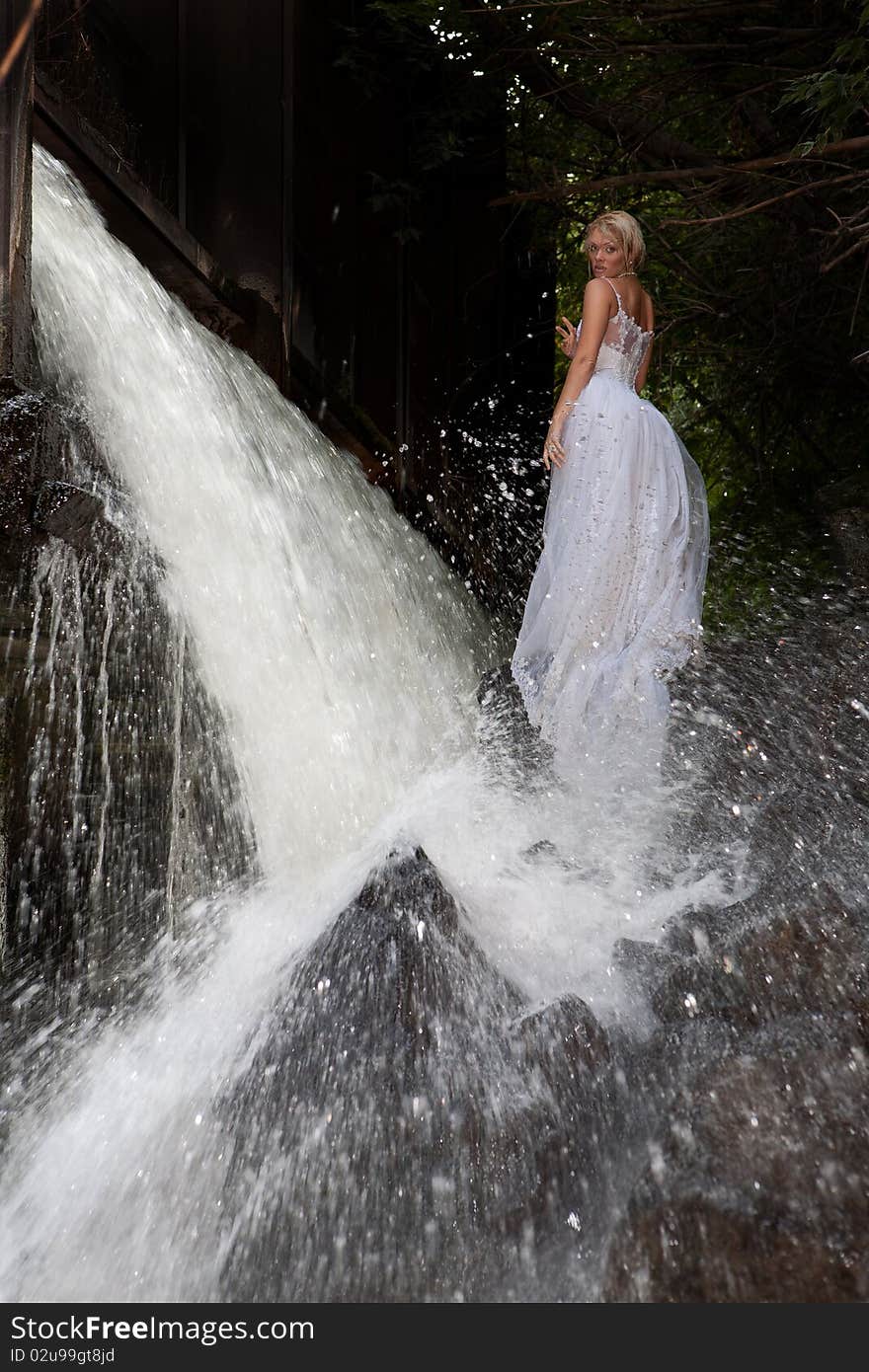 Young blonde woman in a white wedding dress near the waterfall. Young blonde woman in a white wedding dress near the waterfall