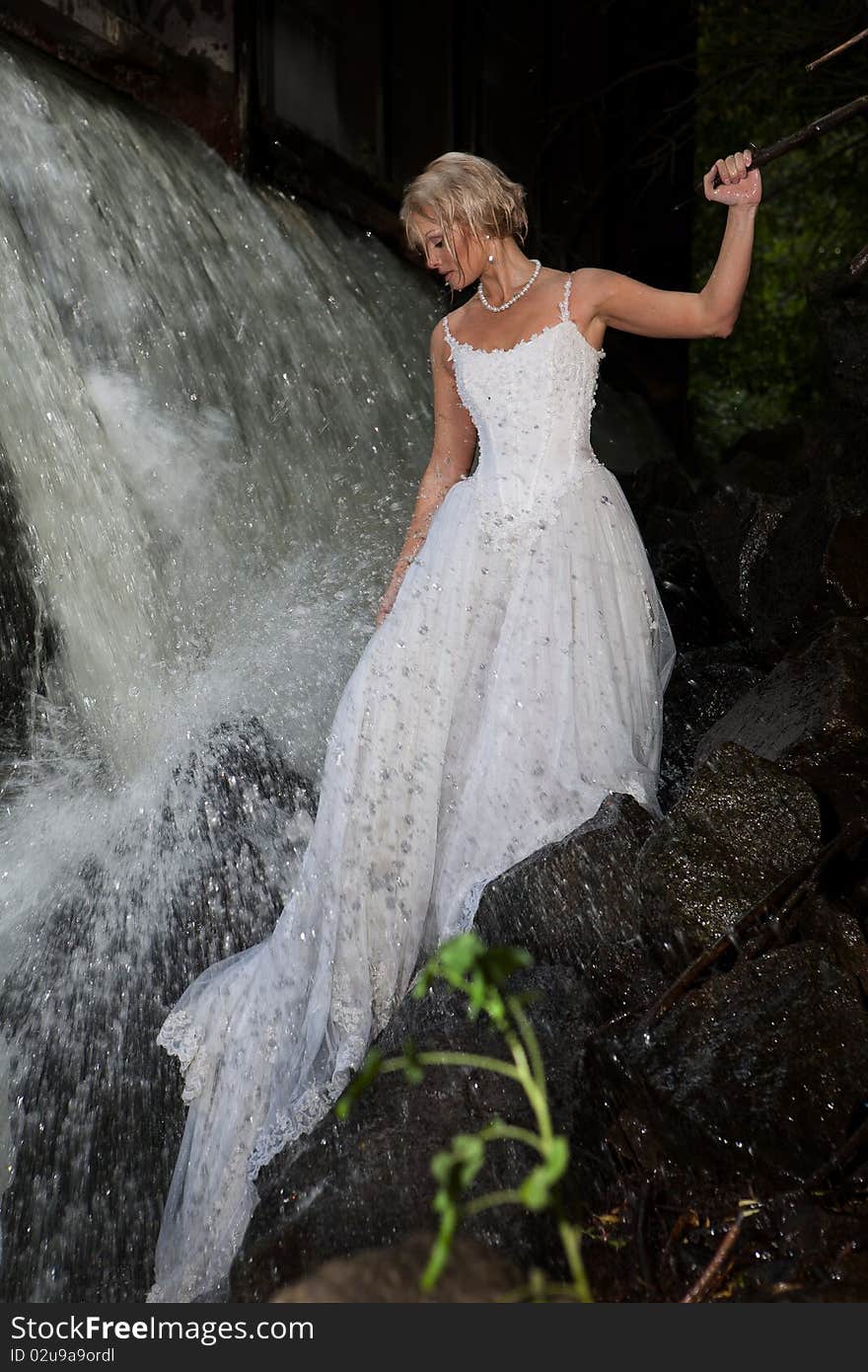 Young blonde woman in a white wedding dress near the waterfall. Young blonde woman in a white wedding dress near the waterfall