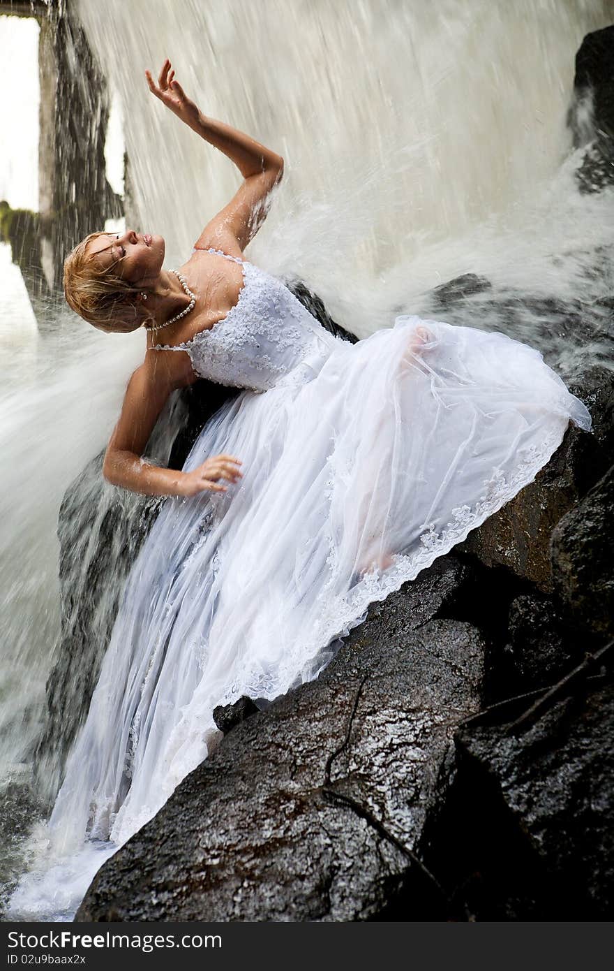 Young blonde woman in a white wedding dress near the waterfall. Young blonde woman in a white wedding dress near the waterfall