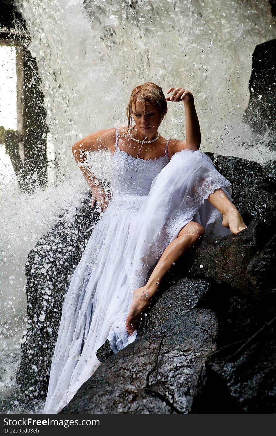 Young blonde woman in a white wedding dress near the waterfall. Young blonde woman in a white wedding dress near the waterfall