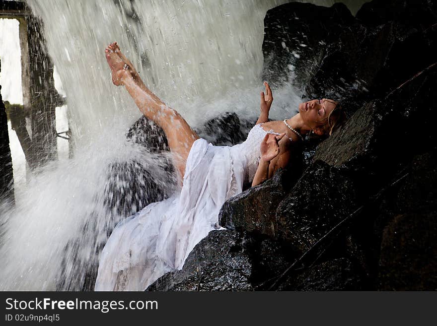 Young blonde woman in a white wedding dress near the waterfall. Young blonde woman in a white wedding dress near the waterfall