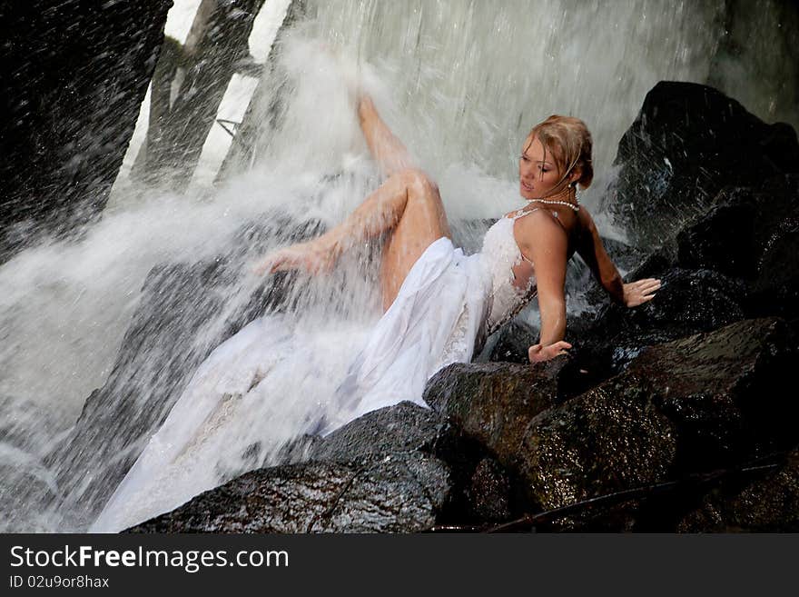 Young blonde woman in a white wedding dress near the waterfall. Young blonde woman in a white wedding dress near the waterfall