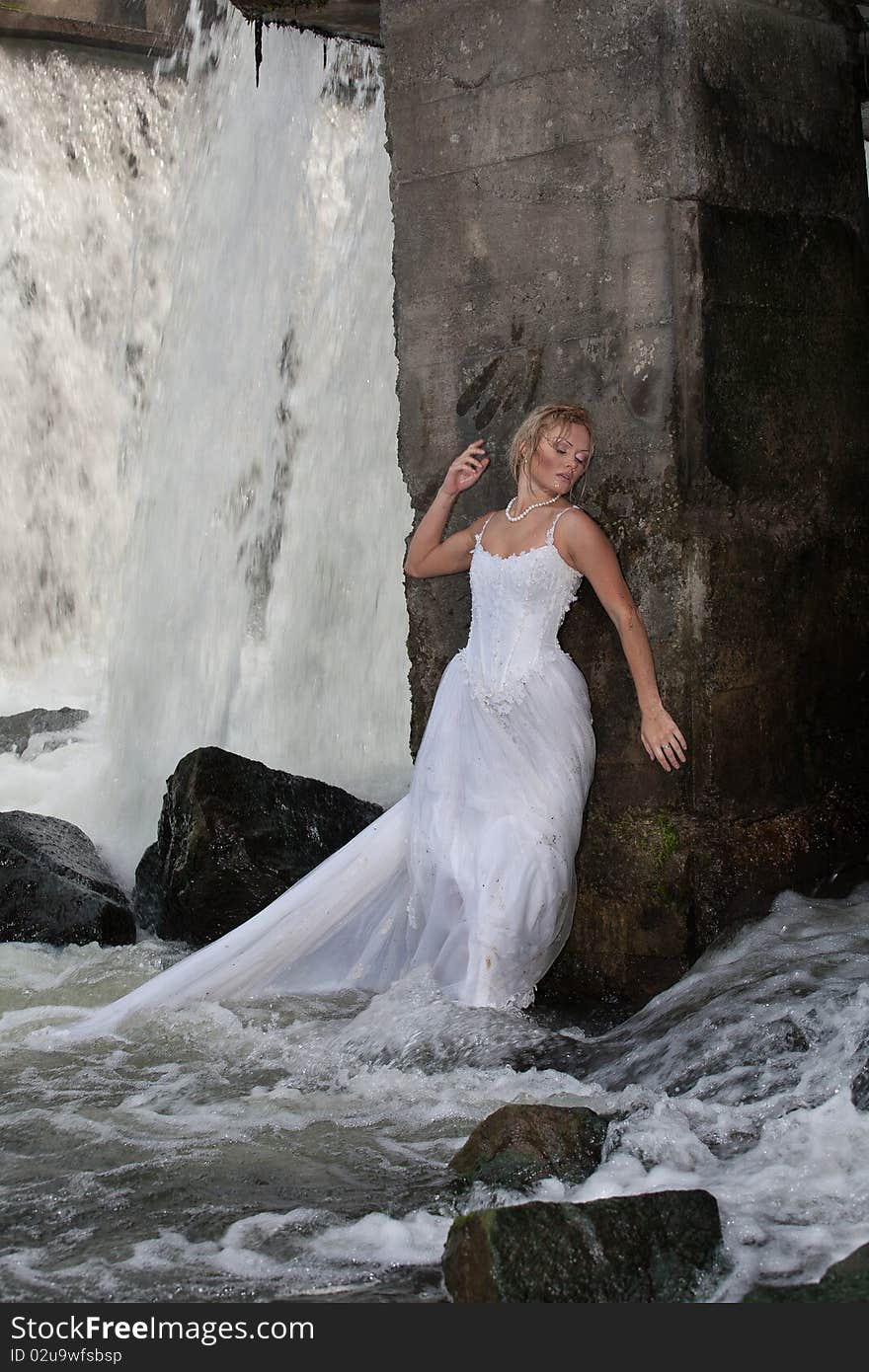 Young blonde woman in a white wedding dress near the waterfall. Young blonde woman in a white wedding dress near the waterfall