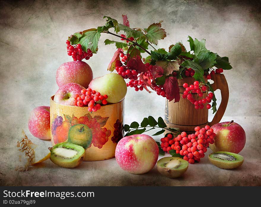 The branches of viburnum cost in a vase alongside apples and kiwi