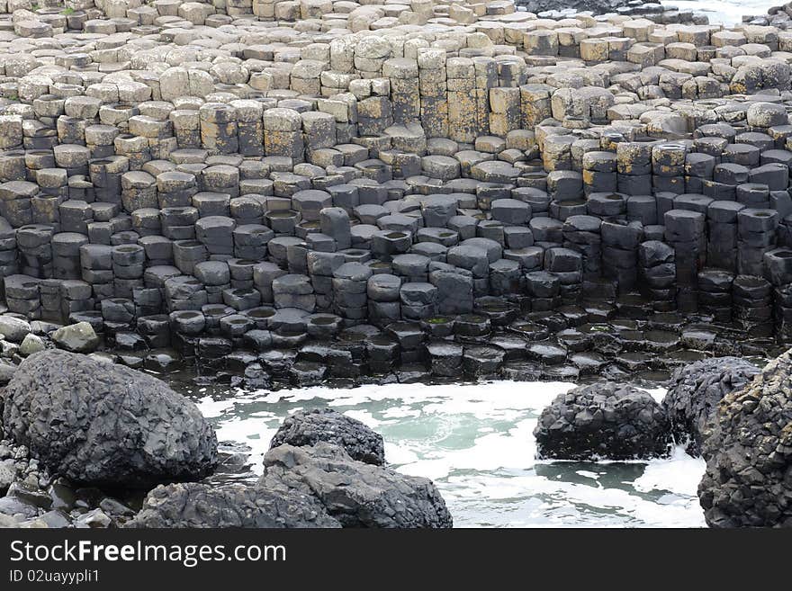 Basalt columns stepping down to the sea with large boulders in the foreground. Basalt columns stepping down to the sea with large boulders in the foreground