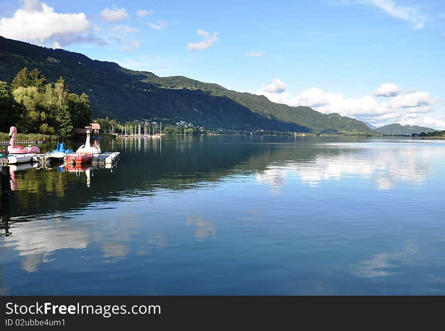 Image shows landscape of Lake Ossiach, Austria, with some pedalos. Image shows landscape of Lake Ossiach, Austria, with some pedalos.