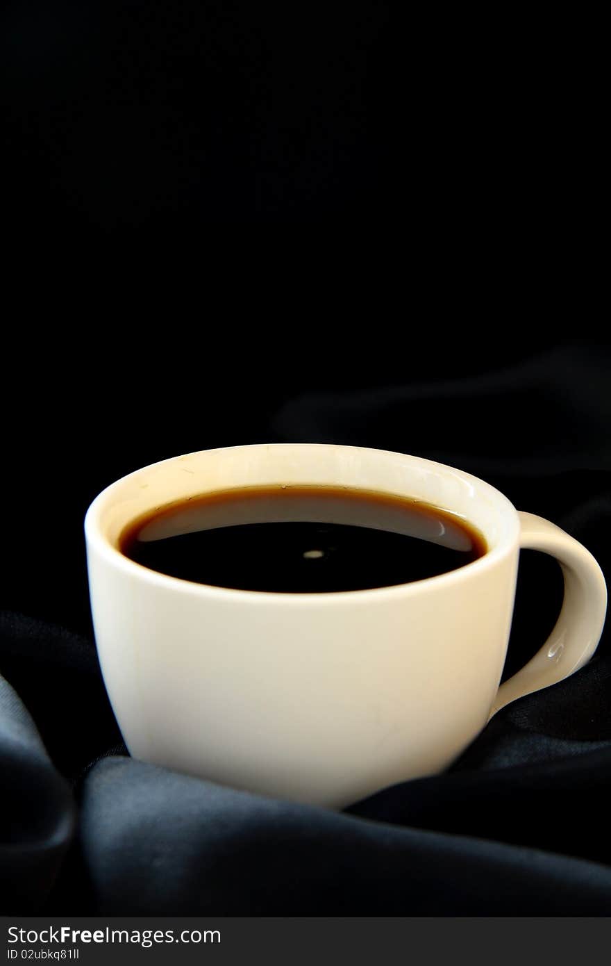 Coffee is poured into a white cup on black silk