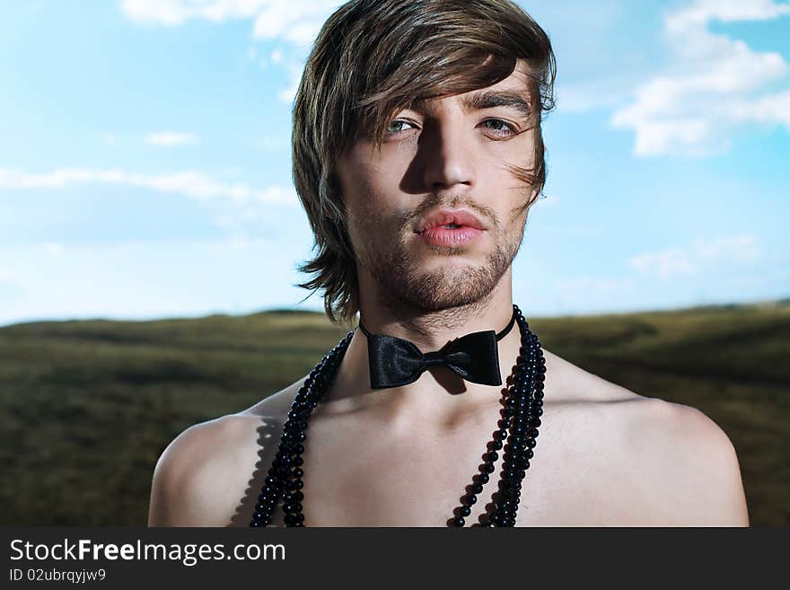 Fashion shot of a handsome young man posing topless in top hat and bow tie over beautiful landscape. Fashion shot of a handsome young man posing topless in top hat and bow tie over beautiful landscape.