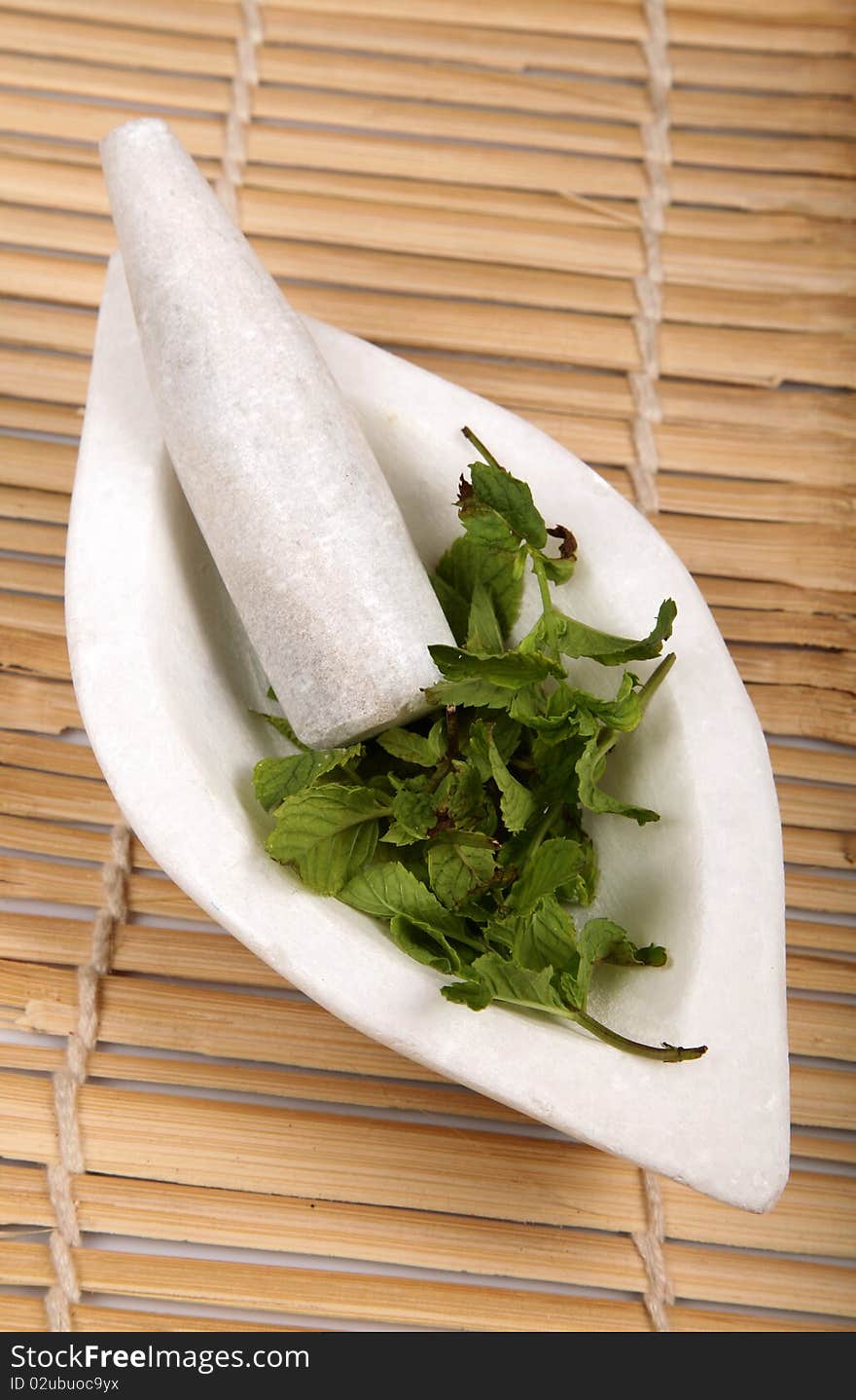 White marble mortar and pestle with mint leaves on wooden background.