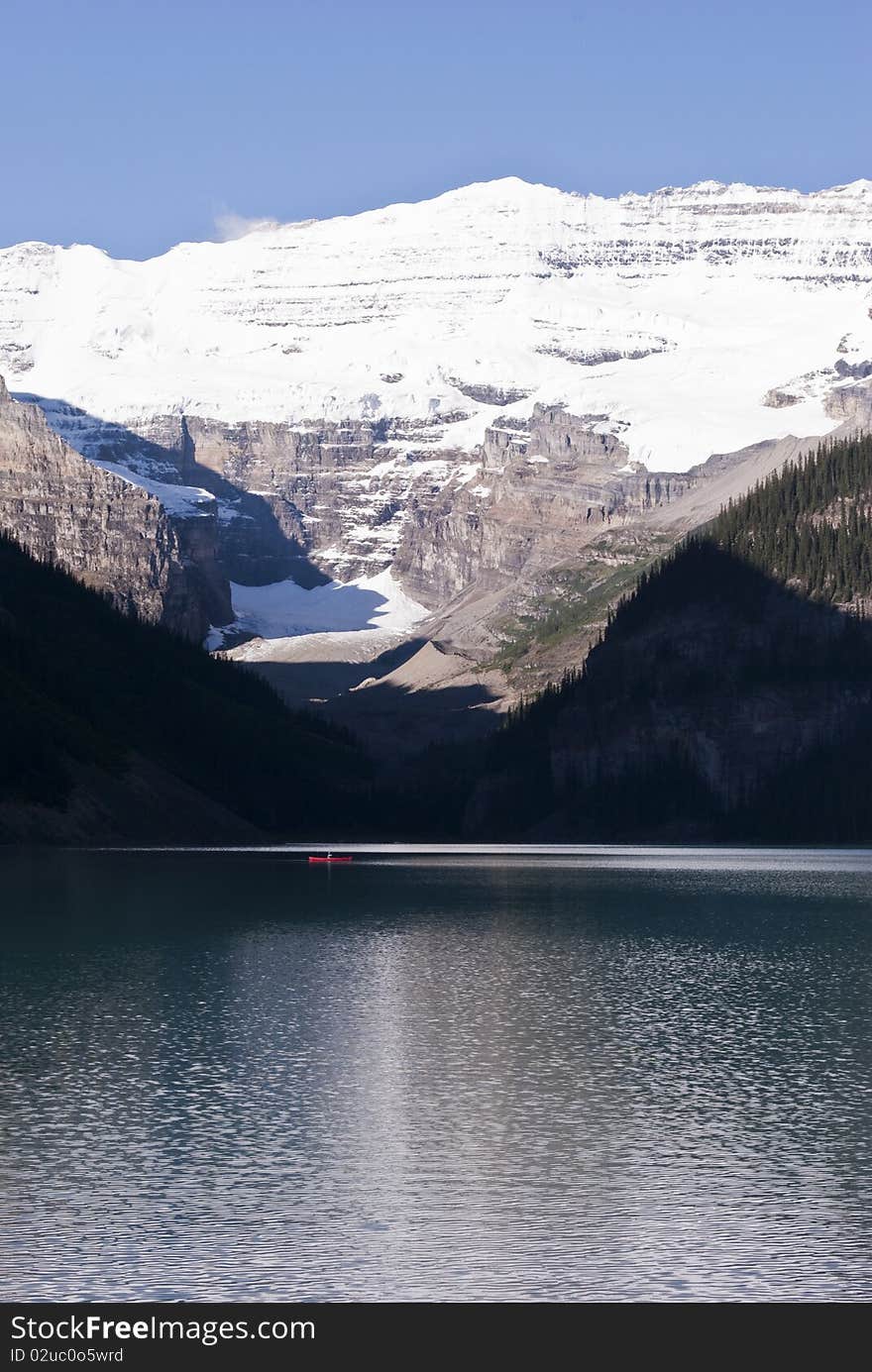 A beautiful blue lake with a person and its canoe under an imponent glacier in the Canadian Rockies. A beautiful blue lake with a person and its canoe under an imponent glacier in the Canadian Rockies