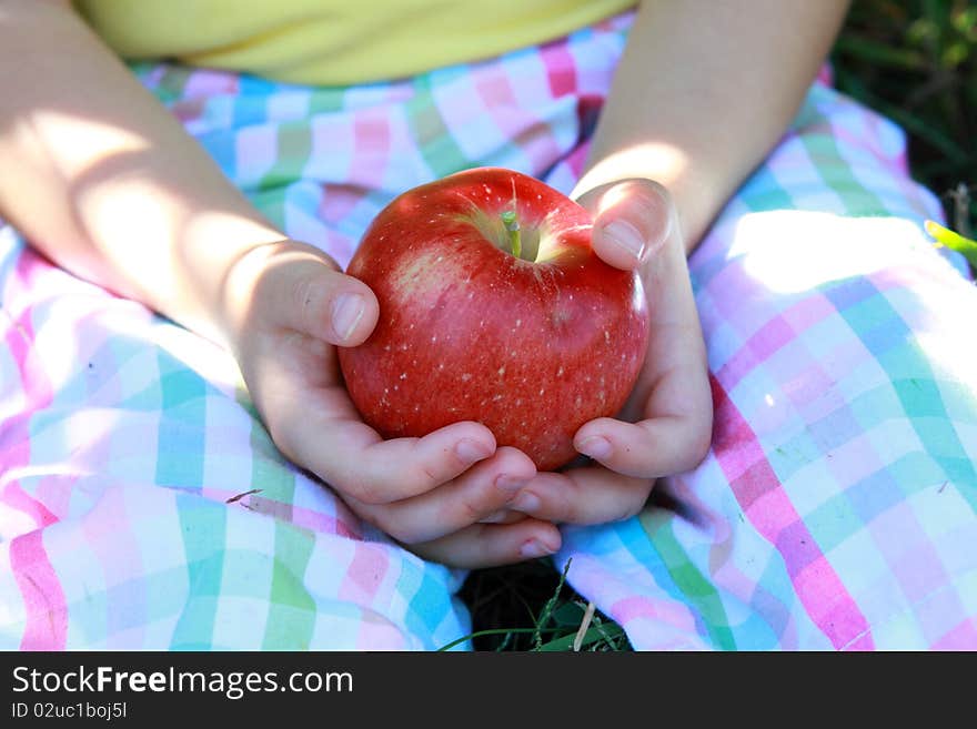 Little girl sitting on a grass and holding red delicious apple. Little girl sitting on a grass and holding red delicious apple