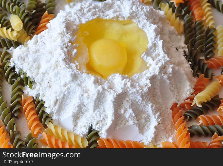 An egg lies in a flour alongside the coloured macaronis. An egg lies in a flour alongside the coloured macaronis