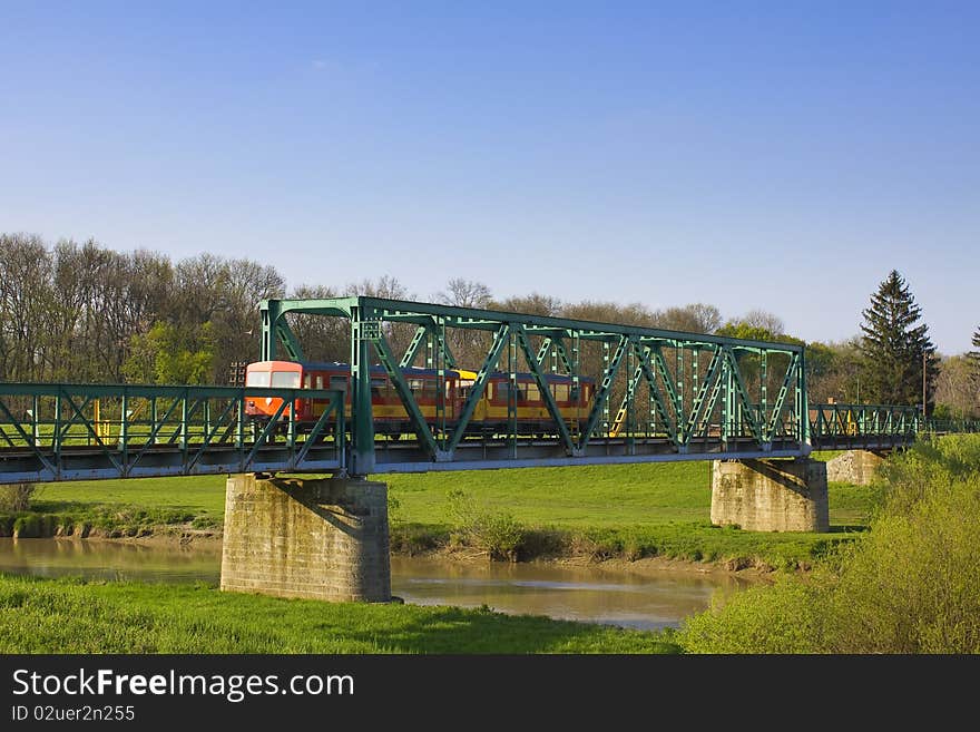 Small, red, urban train passing an old green iron bridge in europe. Small, red, urban train passing an old green iron bridge in europe