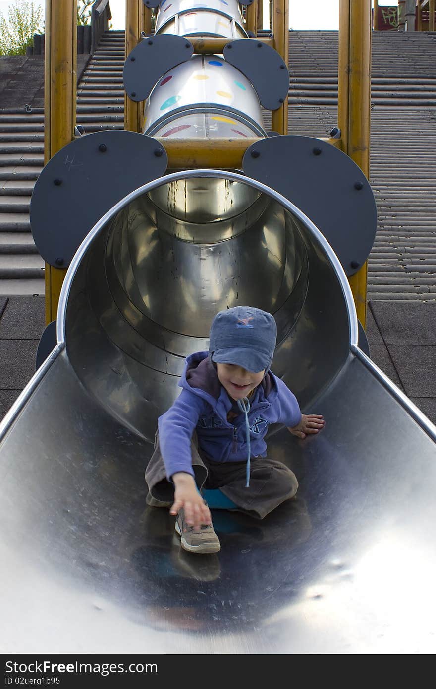 Young boy happily playing on a long slide. Young boy happily playing on a long slide