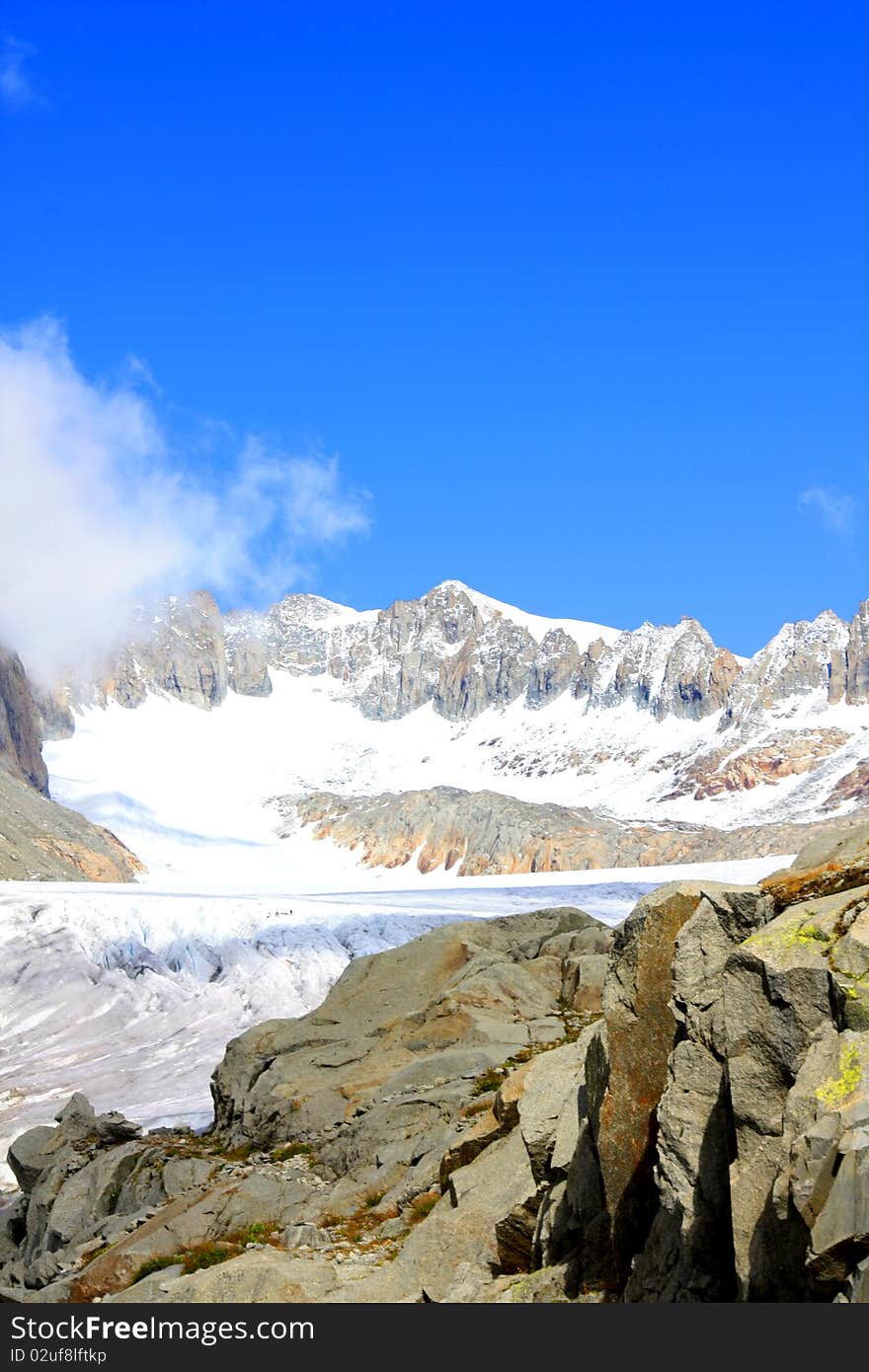 A snow capped mountain in Switzerland overlooking a glacier and a rocky hillside with clouds coming in. A snow capped mountain in Switzerland overlooking a glacier and a rocky hillside with clouds coming in