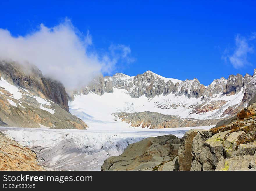 A snow capped mountain in  Switzerland overlooking a glacier and a rocky hillside with clouds coming in. A snow capped mountain in  Switzerland overlooking a glacier and a rocky hillside with clouds coming in