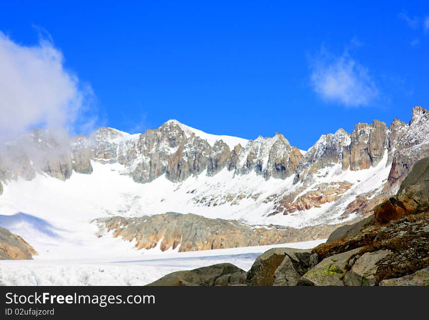 A snow capped mountain in Switzerland and a rocky hillside with clouds coming in. A snow capped mountain in Switzerland and a rocky hillside with clouds coming in