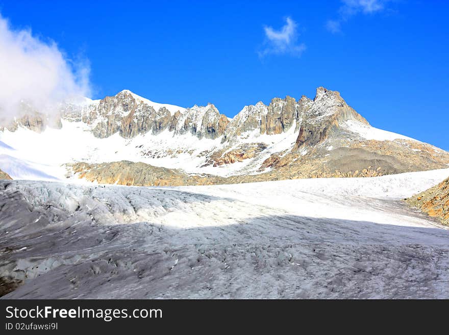 A snow capped mountain in  Switzerland and a rocky hillside with clouds coming in. A snow capped mountain in  Switzerland and a rocky hillside with clouds coming in