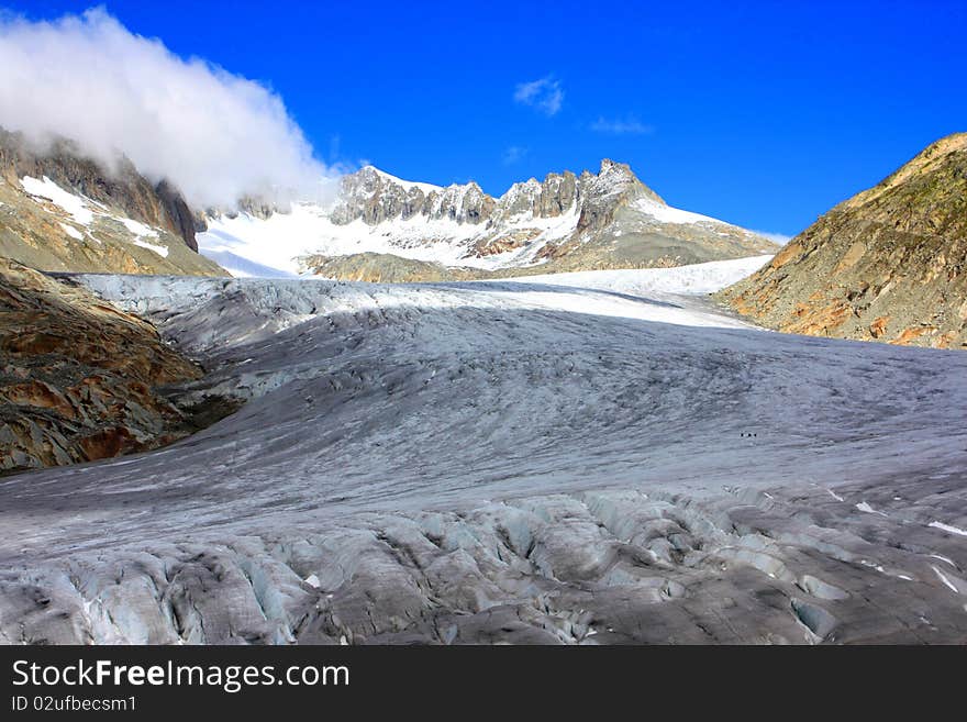 A snow capped mountain in Switzerland and a rocky hillside with clouds coming in over a glacier. A snow capped mountain in Switzerland and a rocky hillside with clouds coming in over a glacier