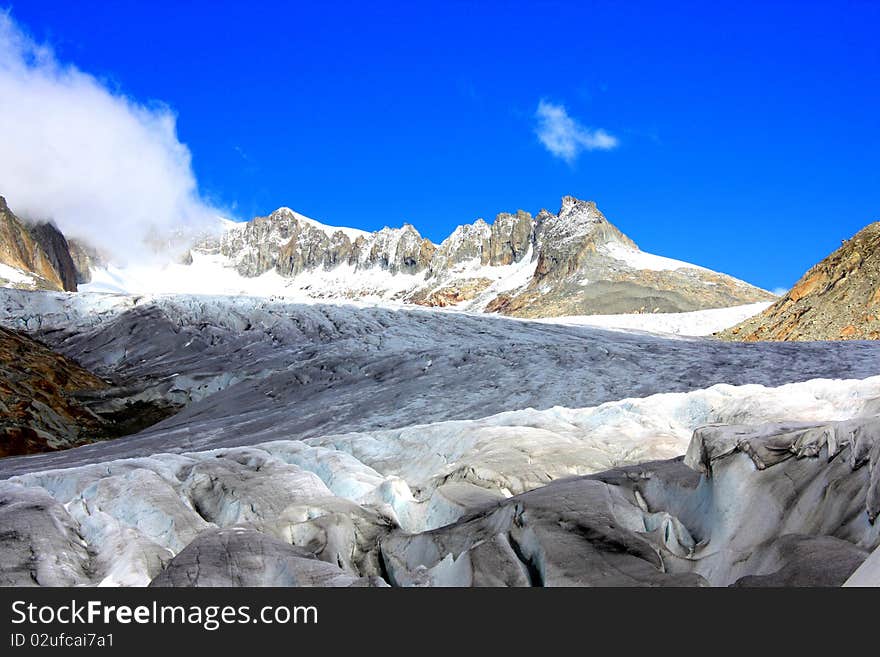 A snow capped mountain in  Switzerland overlooking a glacier and a rocky hillside with clouds coming in near passes in switzerland. A snow capped mountain in  Switzerland overlooking a glacier and a rocky hillside with clouds coming in near passes in switzerland