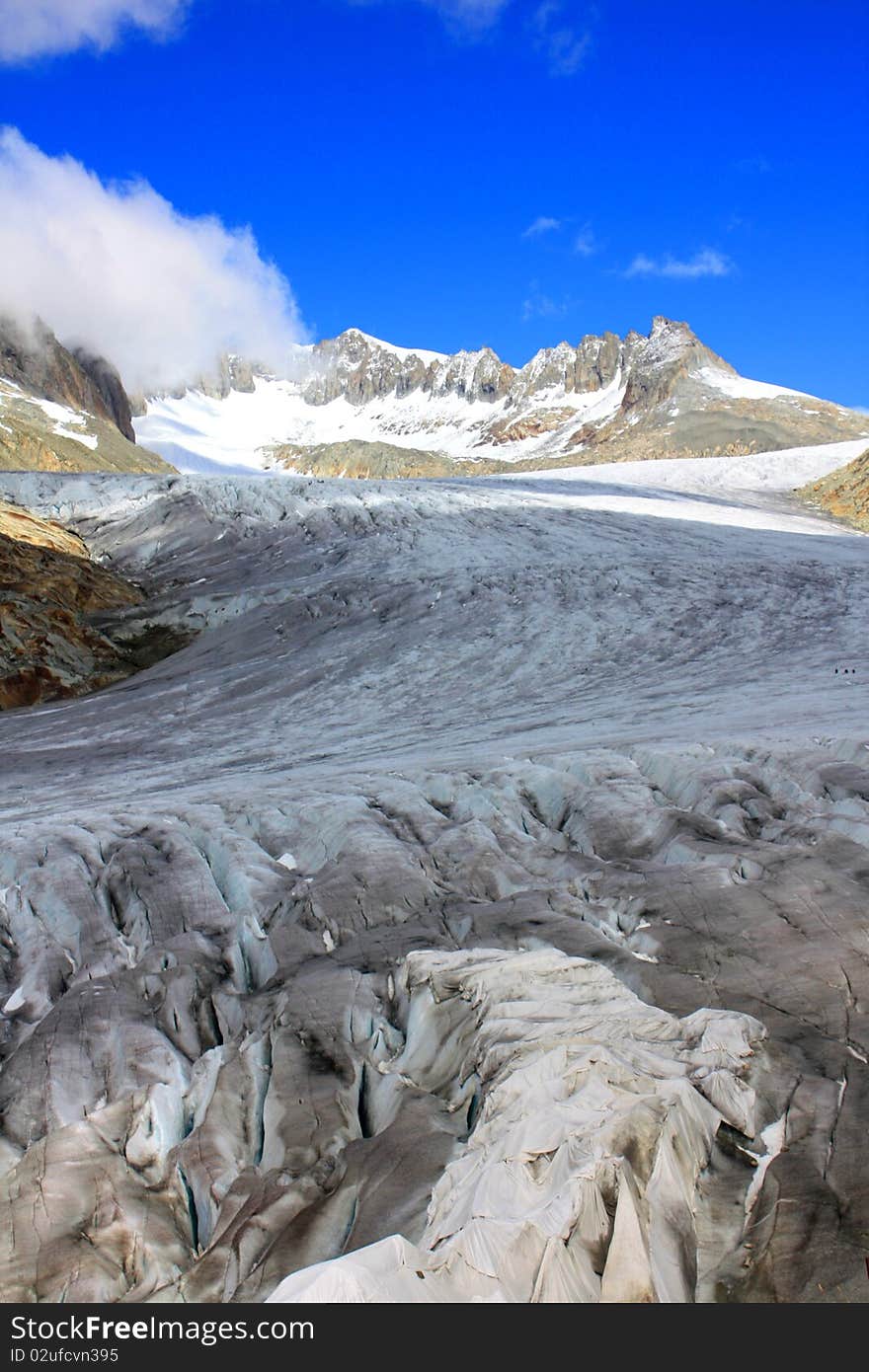 A snow capped mountain in Switzerland overlooking a glacier and a rocky hillside with clouds coming in with a focus on the glacier in a portrait photo. A snow capped mountain in Switzerland overlooking a glacier and a rocky hillside with clouds coming in with a focus on the glacier in a portrait photo