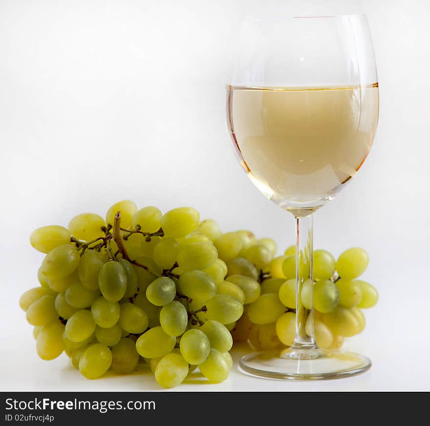 There are glass of white wine and grapes on a white background