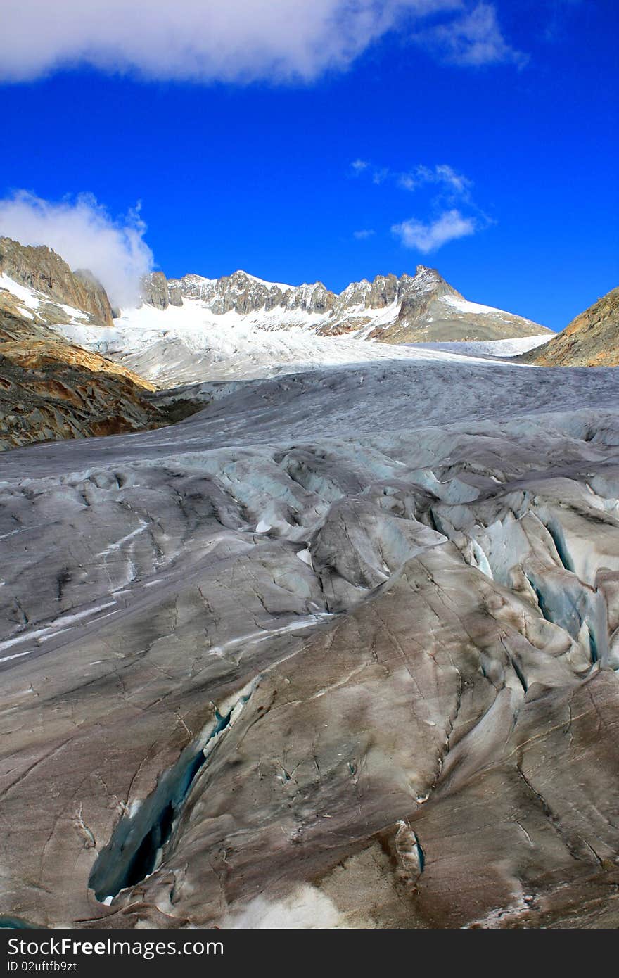 A Glacier showing a crack with snow covered mountains under a blue sunny sky and clouds. A Glacier showing a crack with snow covered mountains under a blue sunny sky and clouds