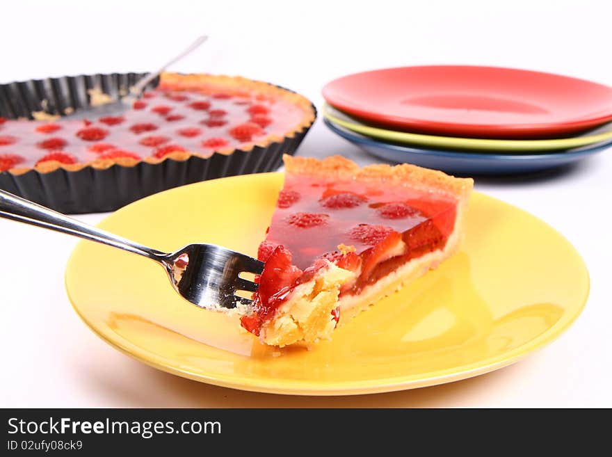 Piece of Strawberry Tart on a yellow plate a tart panand plates in the background and some of the tart on a fork