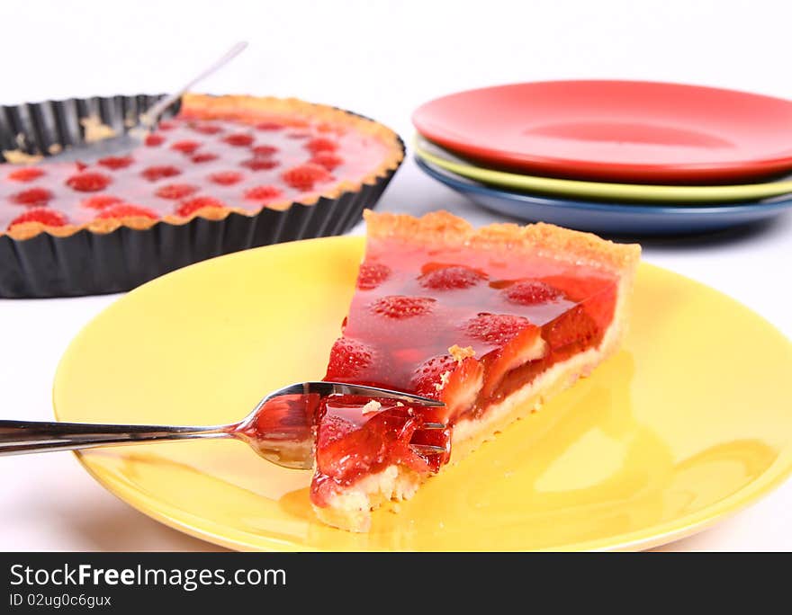 Piece of Strawberry Tart on a yellow plate being eaten with a fork, a tart pan and plates in the background