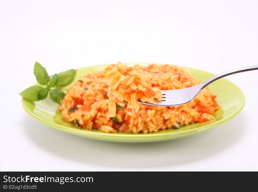 Risotto with tomatoes on a green plate decorated with basil being eaten with a fork