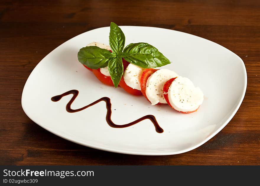 Italian caprese made of tomato, mozzarella and basil putted on a wood table. Italian caprese made of tomato, mozzarella and basil putted on a wood table