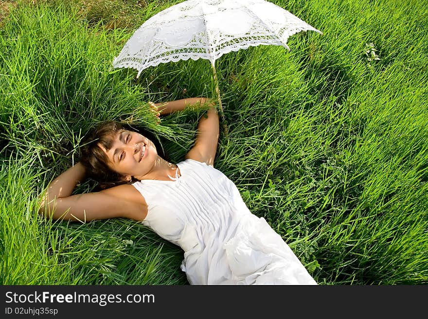 Young pretty lady in white dress and with umblella having a rest on the green meadow. Young pretty lady in white dress and with umblella having a rest on the green meadow