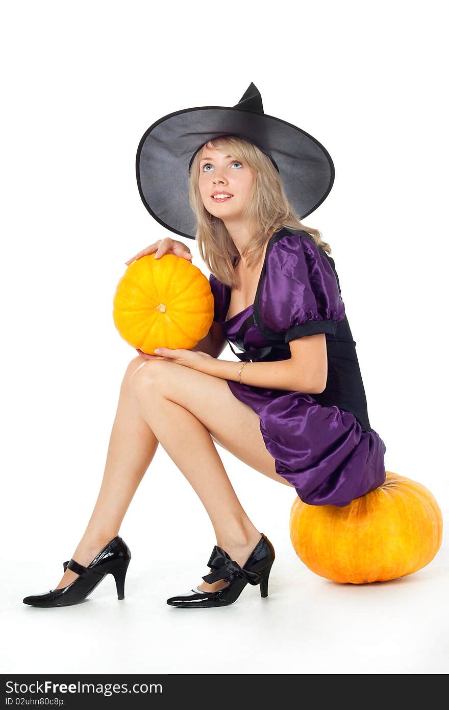 Young blonde witch sitting on a pumpkin, holding a pumpkin