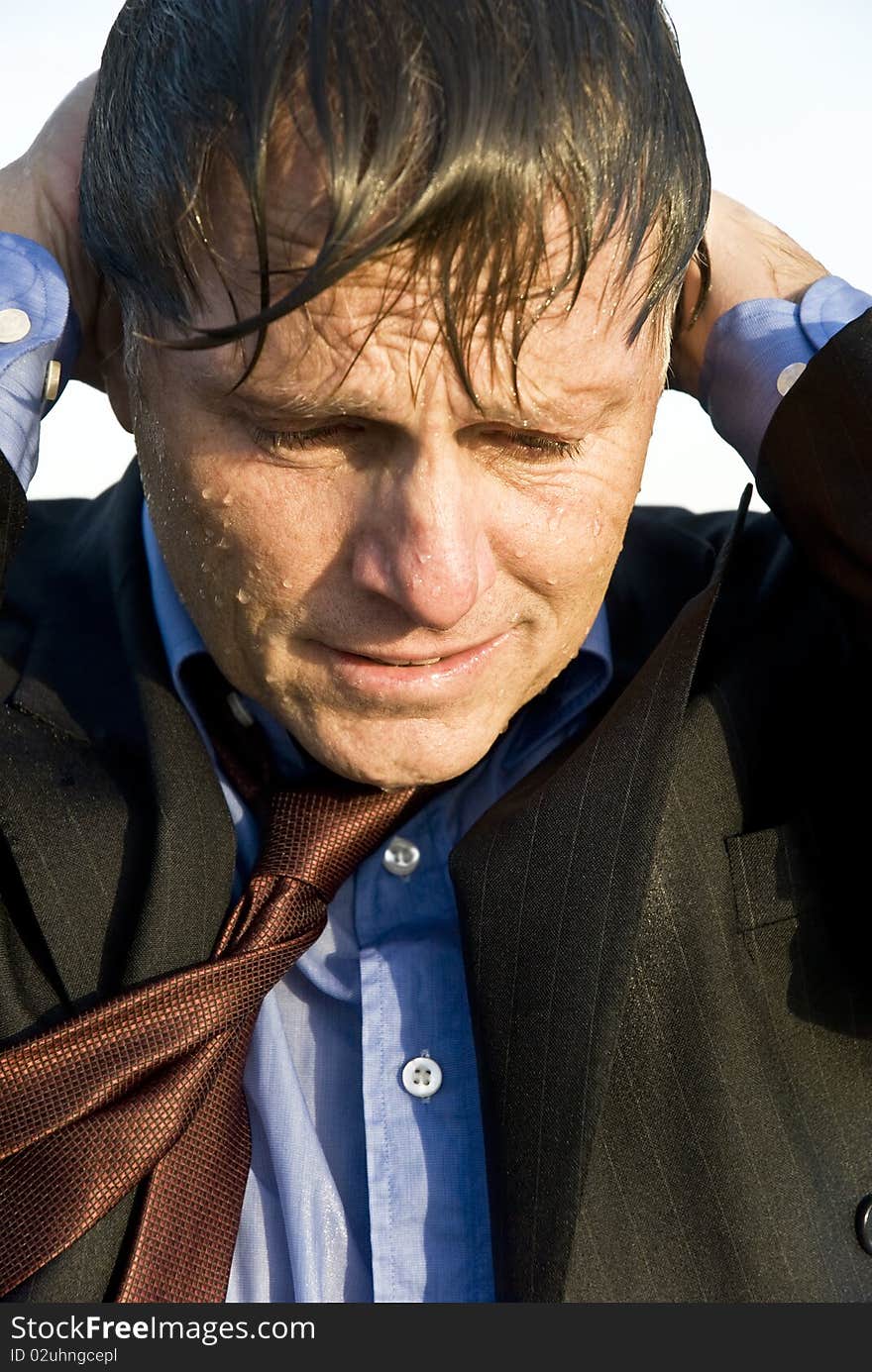 Color portrait photo of an anxious and depressed businessman who is soaking wet and with his hands behind his head. Color portrait photo of an anxious and depressed businessman who is soaking wet and with his hands behind his head.