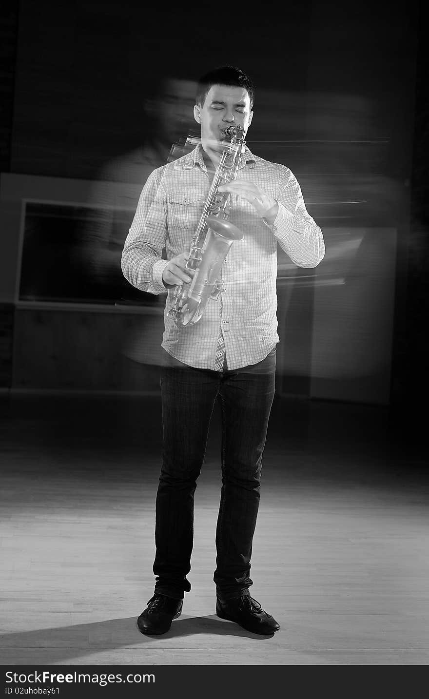 Young handsome man playing music on saxophone. black background