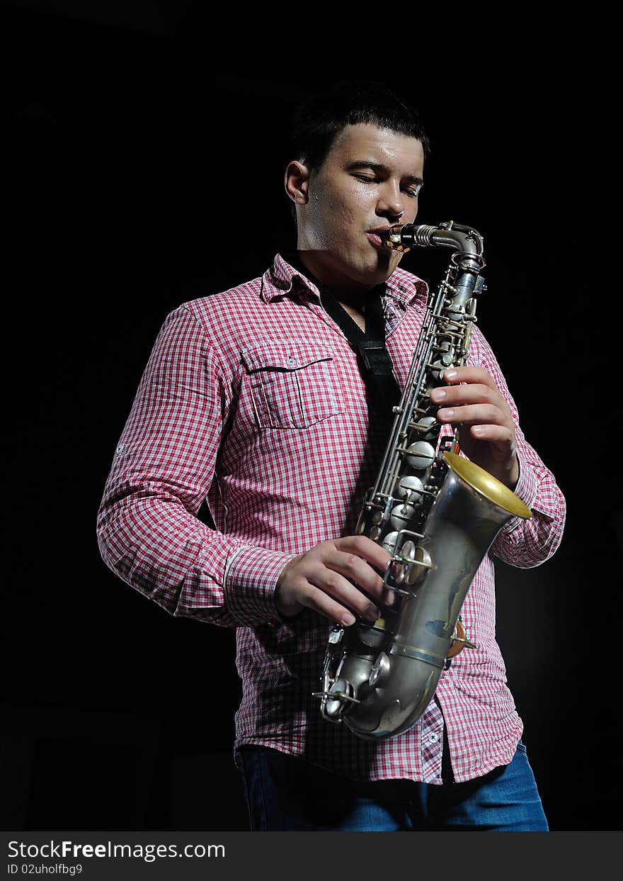 Young handsome man playing music on saxophone. black background