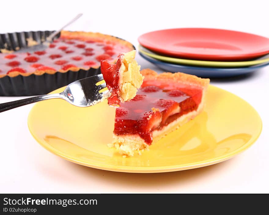 Piece of Strawberry Tart on a yellow plate, a tart pan and plates in the background, and some of the tart on a fork