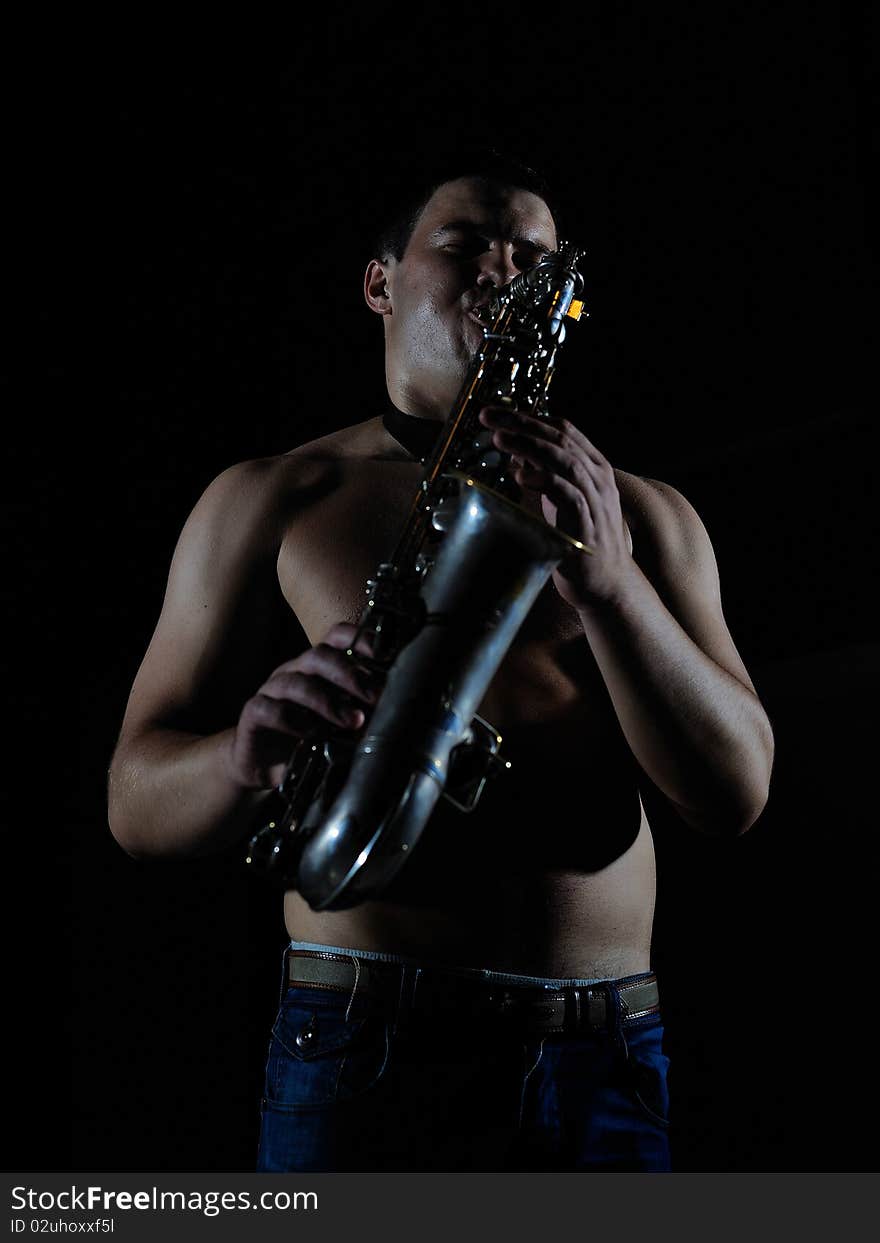 Young handsome man playing music on saxophone. black background