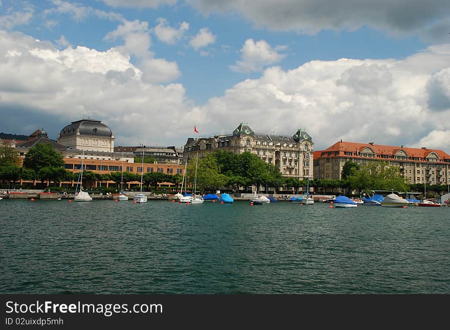 Uto-Quai with its historical buildingd seen from Zurich see port, deep turquoise water of the zurich lake and some yachts are at foreground and th sky conered with rainy clouds is at background. Uto-Quai with its historical buildingd seen from Zurich see port, deep turquoise water of the zurich lake and some yachts are at foreground and th sky conered with rainy clouds is at background