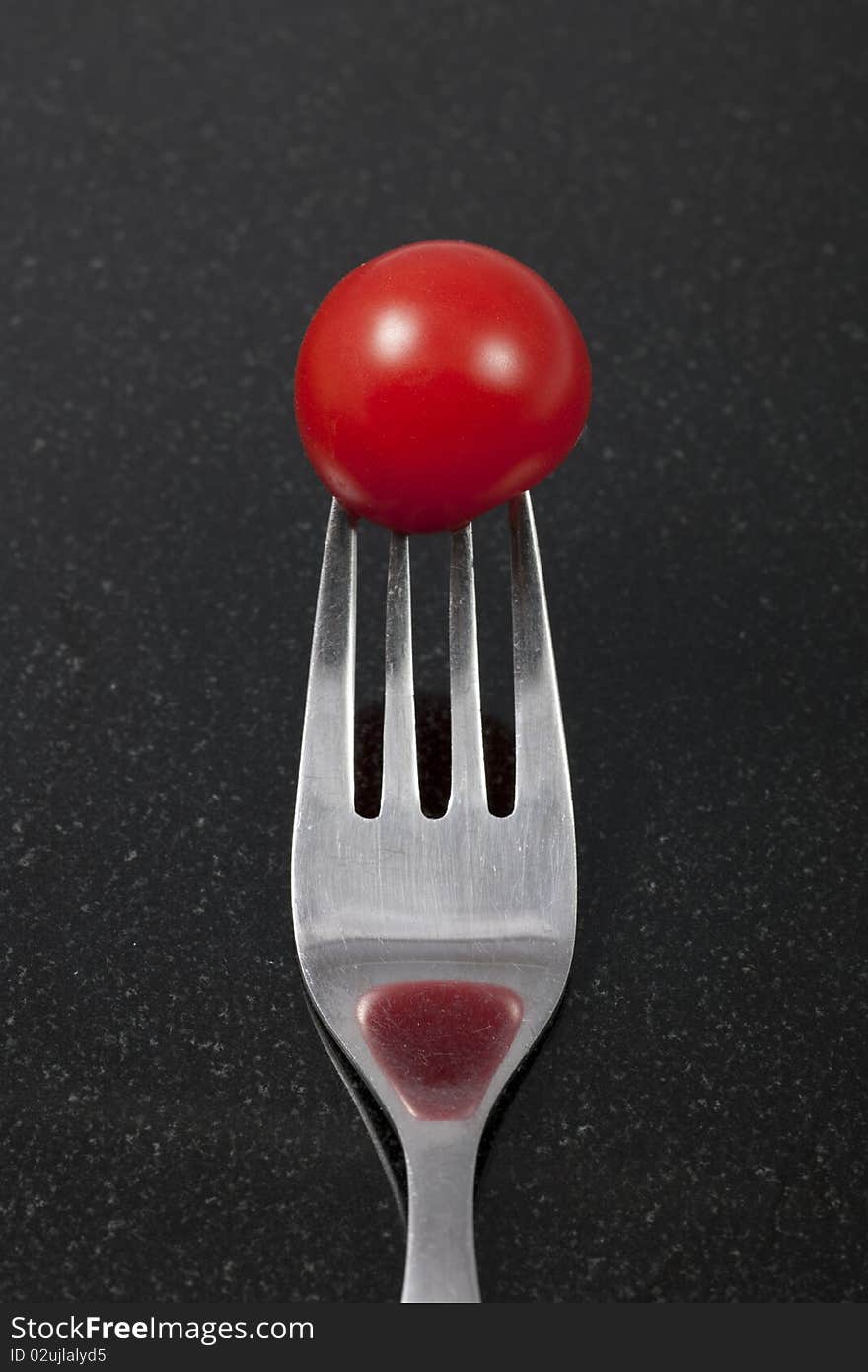 Tomato on a fork with reflection. On a black granite counter. Note: Differential focus.