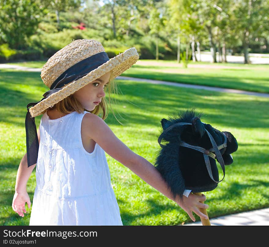 Little girl wearing straw hat and holding her toy pony. Little girl wearing straw hat and holding her toy pony