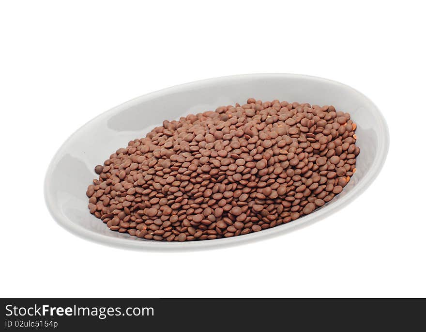 Brown uncooked lentils on plate isolated over white background