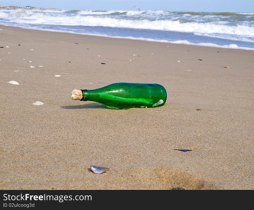 The closed bottle of green color with a note in it lies on seacoast on sand. The closed bottle of green color with a note in it lies on seacoast on sand