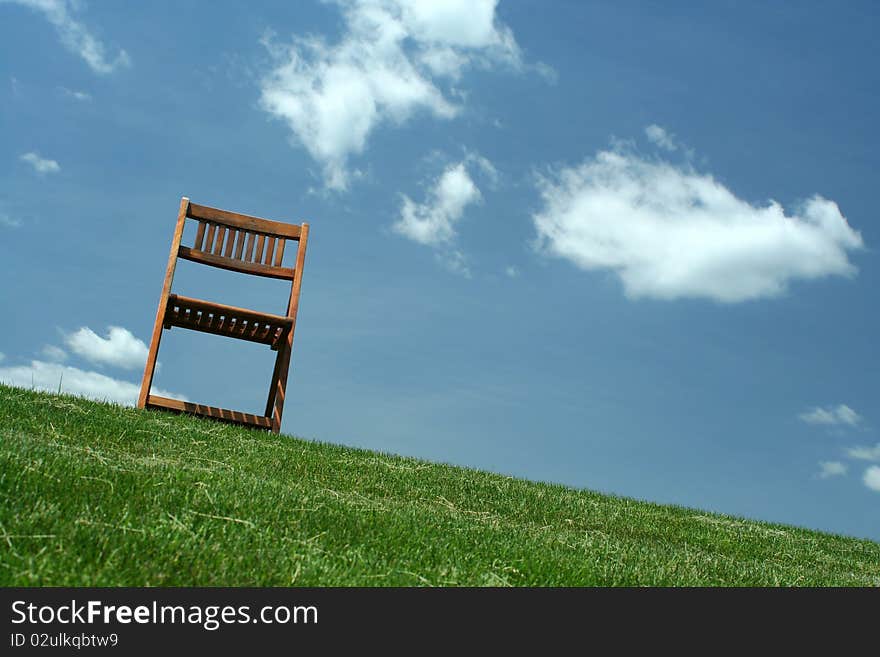 A Wooden chair with grass and sky. A Wooden chair with grass and sky