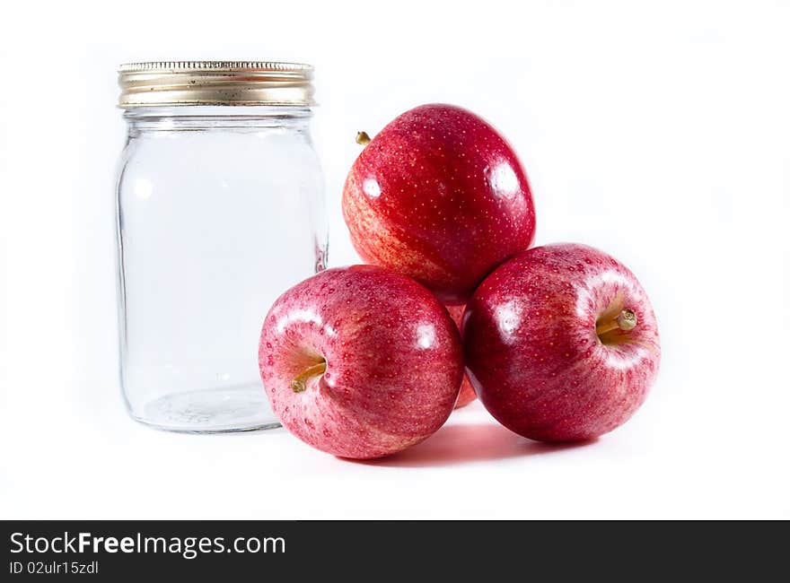 Three red gala apples pilled beside a glass mason jar with metal lid on a white isolated bacground. Three red gala apples pilled beside a glass mason jar with metal lid on a white isolated bacground.