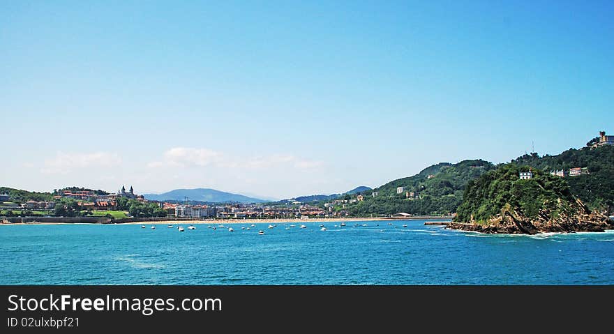 We can see a landscape in spain, a seascape, with the beach, and little islands, like big rocs; little boats, blue sky and many nature and urbanism. We can see a landscape in spain, a seascape, with the beach, and little islands, like big rocs; little boats, blue sky and many nature and urbanism.