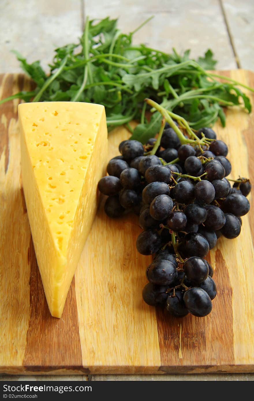 Black grapes and cheese with herbs on a wooden board