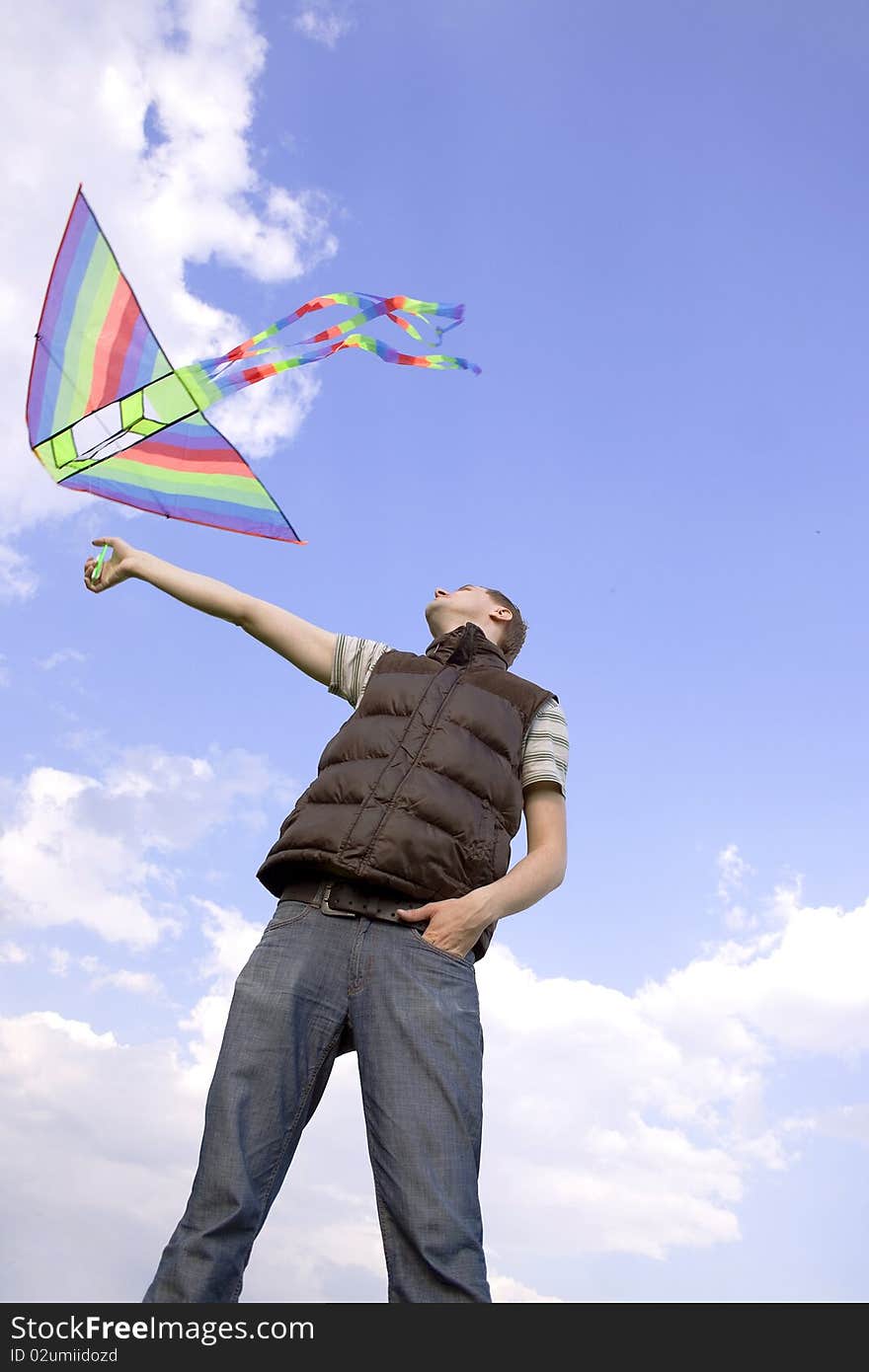 Young man playing with multicolored kite and looking on it, view from below