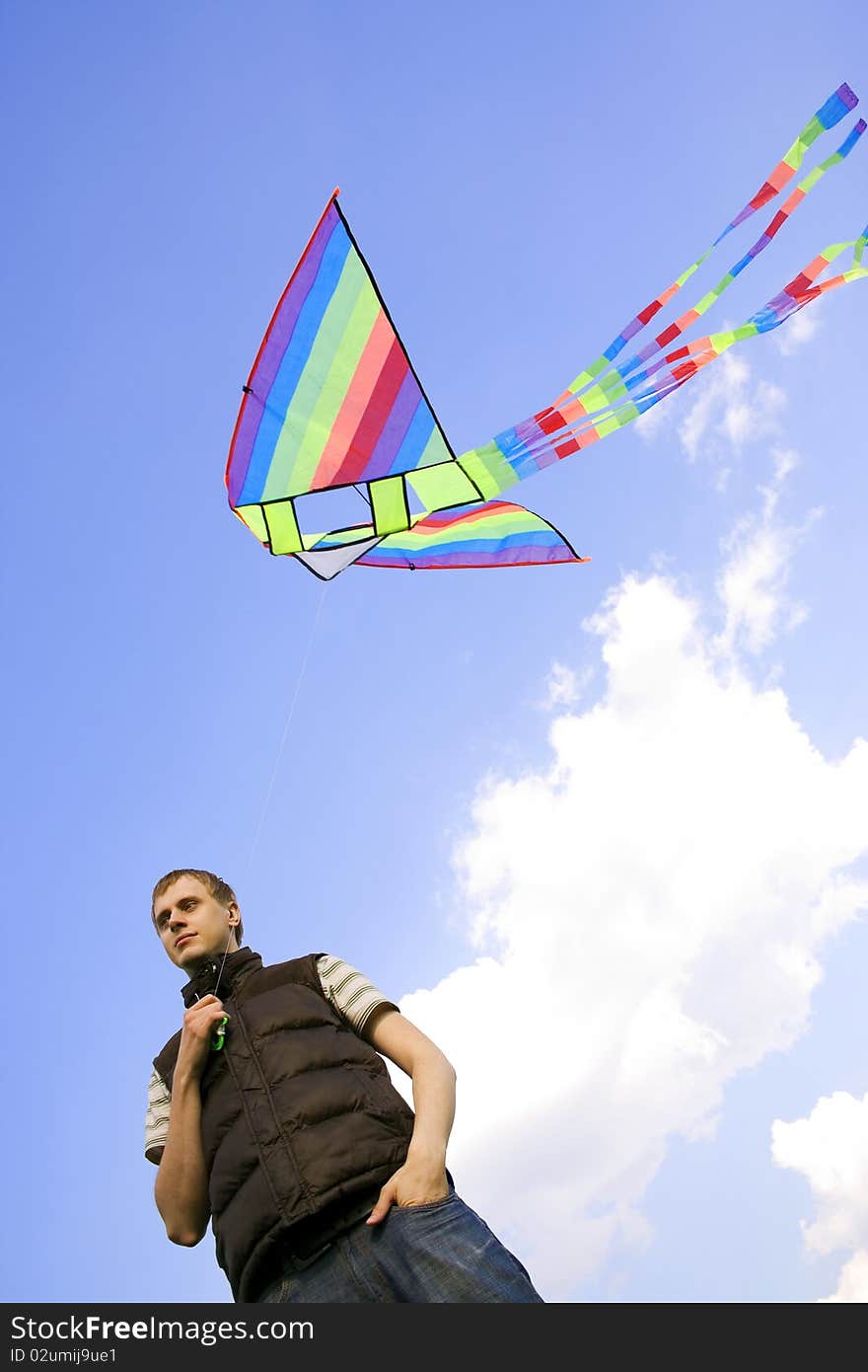 Young man playing with multicolored kite and looking at side, view from below